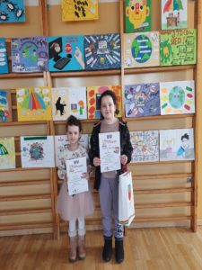 Nagrodzone dziewczynki na tle prac w Gminnym Konkursie Plastycznym